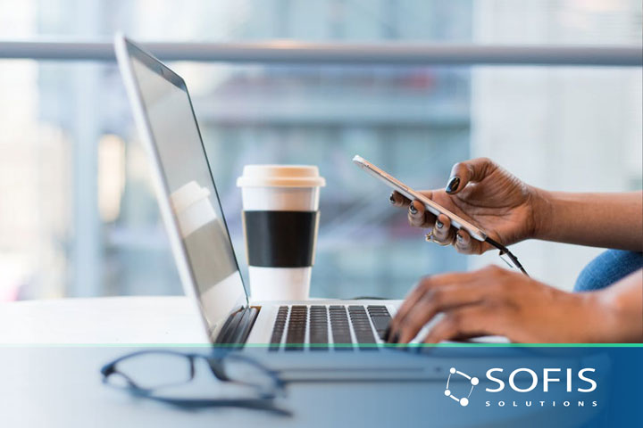 Persona frente a computadora y con un celular en la mano.